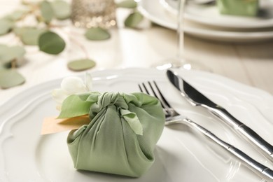 Photo of Furoshiki technique. Gift packed in green fabric with flower and blank card on table, closeup