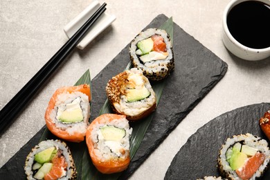 Photo of Delicious sushi rolls, soy sauce and chopsticks on light grey table, above view