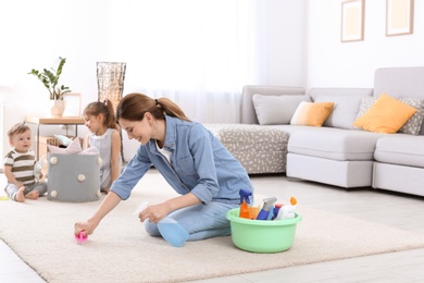 Photo of Housewife cleaning carpet while her children playing in room
