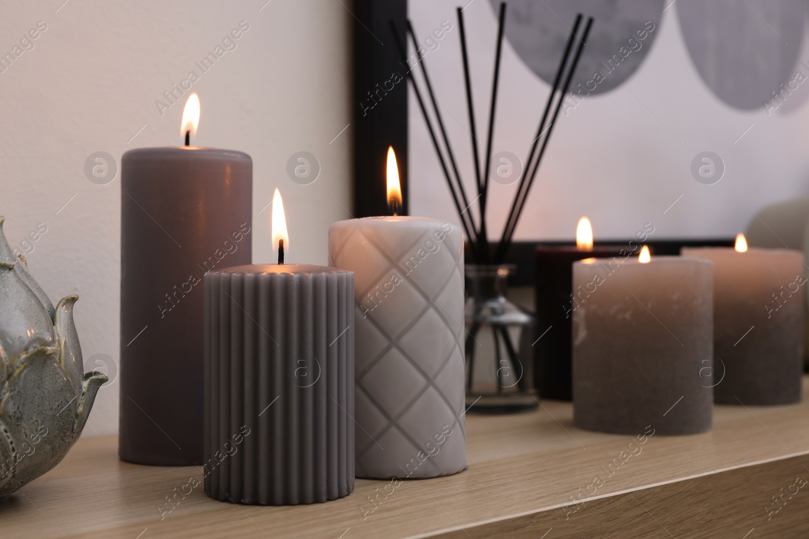 Photo of Burning candles and air freshener on wooden shelf indoors