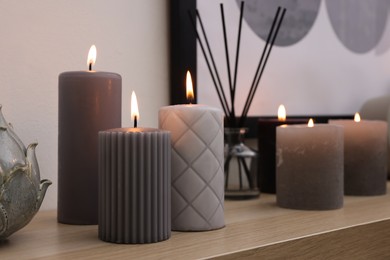 Burning candles and air freshener on wooden shelf indoors