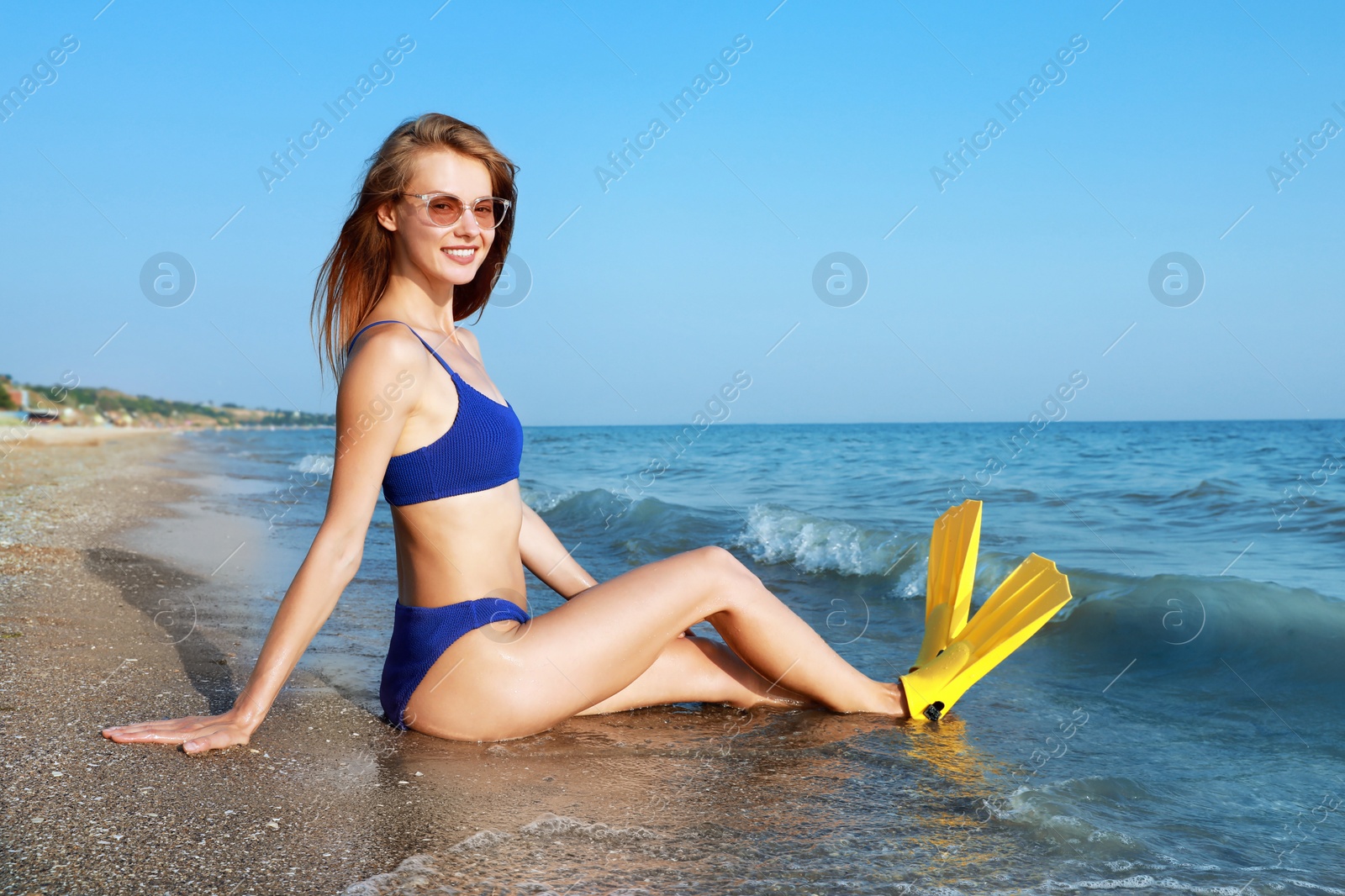 Photo of Happy woman in flippers sitting near sea on beach