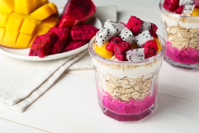 Photo of Glass of granola with pitahaya, yogurt and mango on white wooden table, space for text