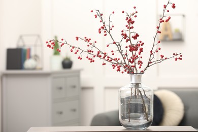 Photo of Hawthorn branches with red berries on table in living room, space for text