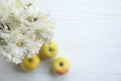 Photo of Beautiful chrysanthemum flowers and ripe apples on white wooden table, flat lay. Space for text