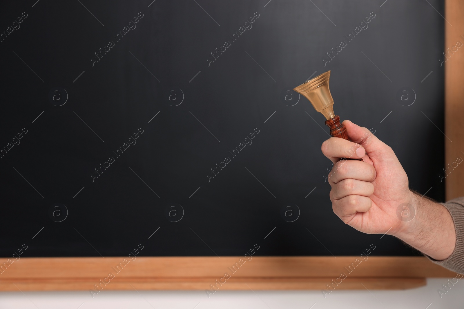 Photo of Teacher with school bell near black chalkboard, closeup. Space for text