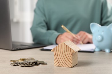 Woman planning budget at wooden table, focus on house model and coins