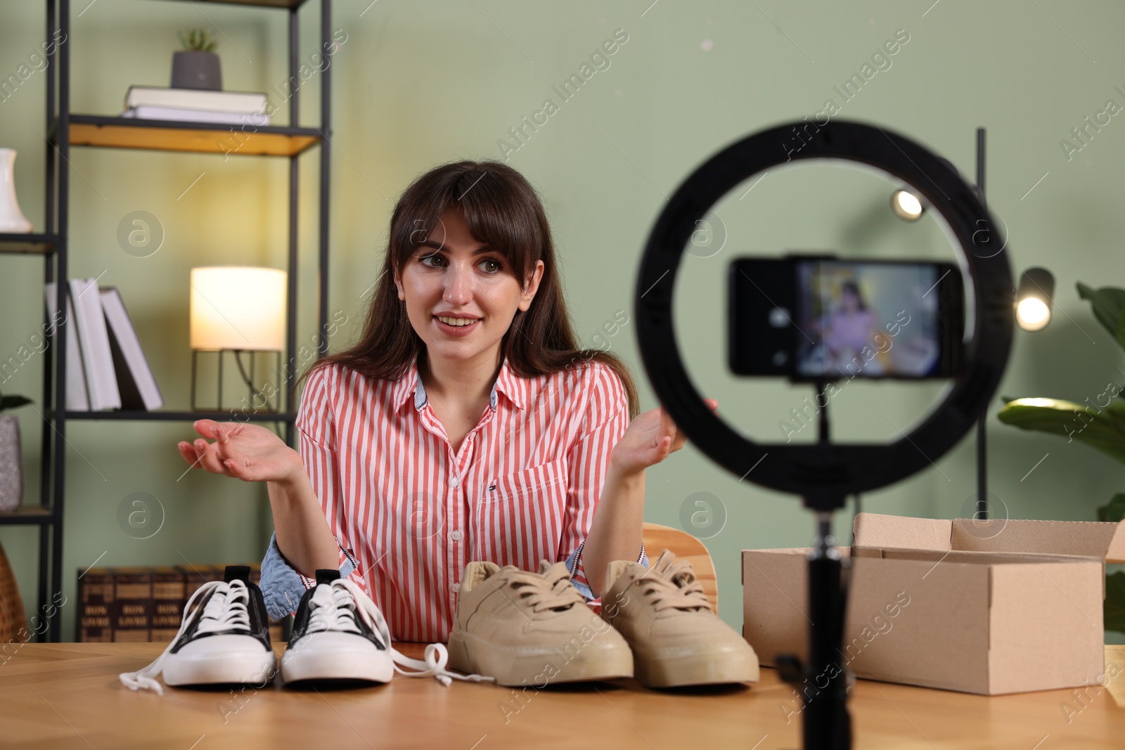 Photo of Smiling fashion blogger recording video while talking about sneakers at home