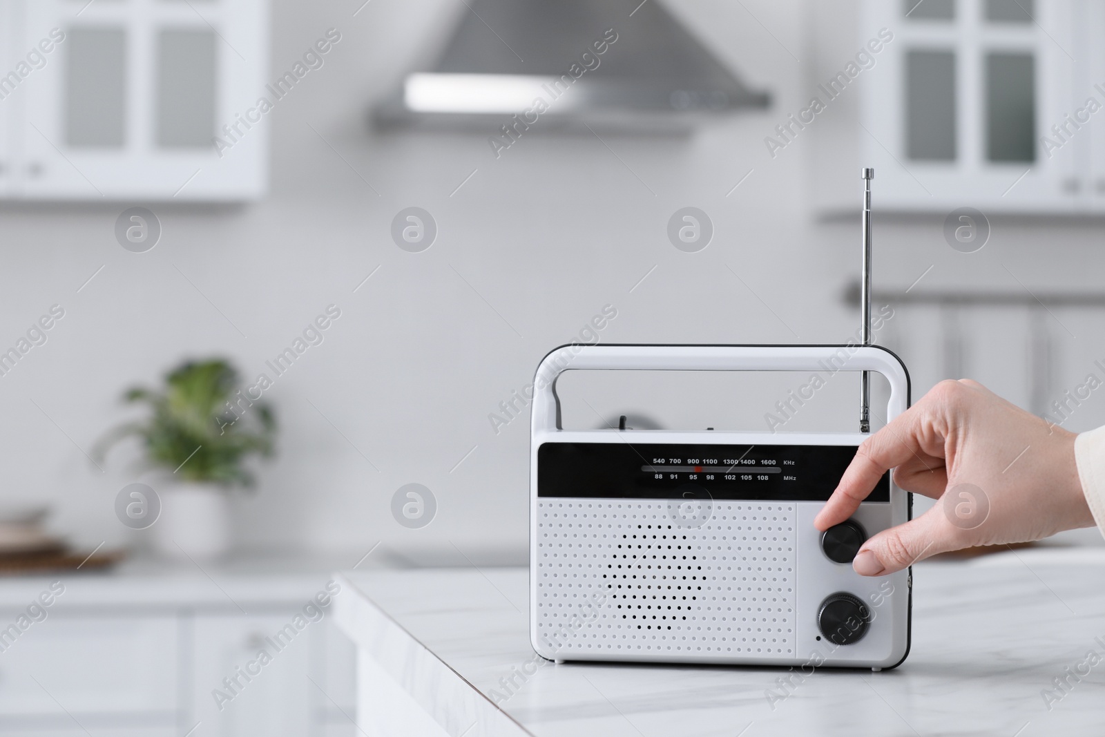 Photo of Woman turning volume knob on radio in kitchen, closeup. Space for text