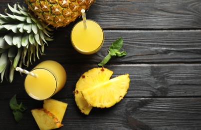 Photo of Delicious pineapple juice and fresh fruit on black wooden table, flat lay. Space for text