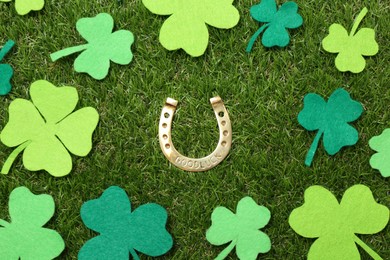 Photo of St. Patrick's day. Golden horseshoe surrounded by felt clover leaves on green grass, flat lay
