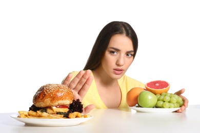 Photo of Woman choosing between fruits and burger with French fries on white background