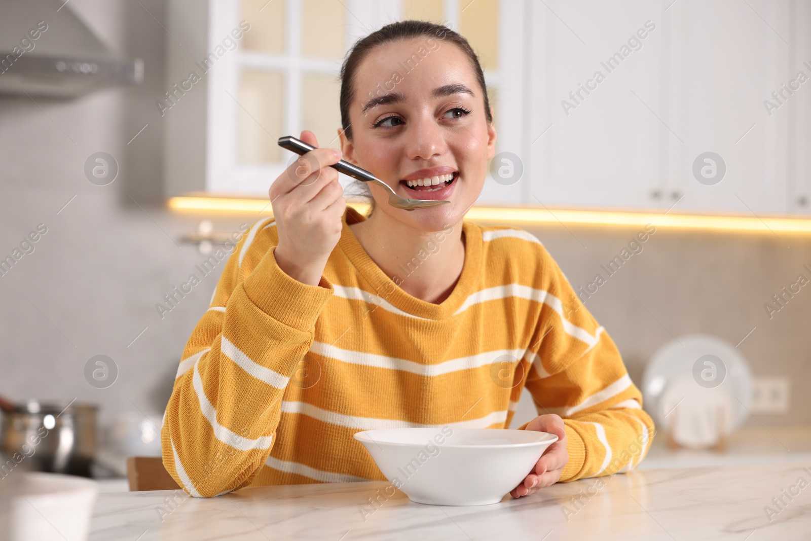 Photo of Woman eating tasty soup at white table in kitchen