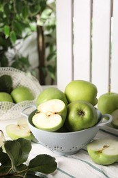 Fresh green apples with water drops and leaves on white striped tablecloth, closeup