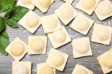 Photo of Uncooked ravioli and basil on wooden table, flat lay