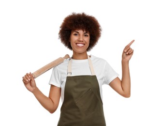 Happy young woman in apron holding rolling pin and pointing at something on white background