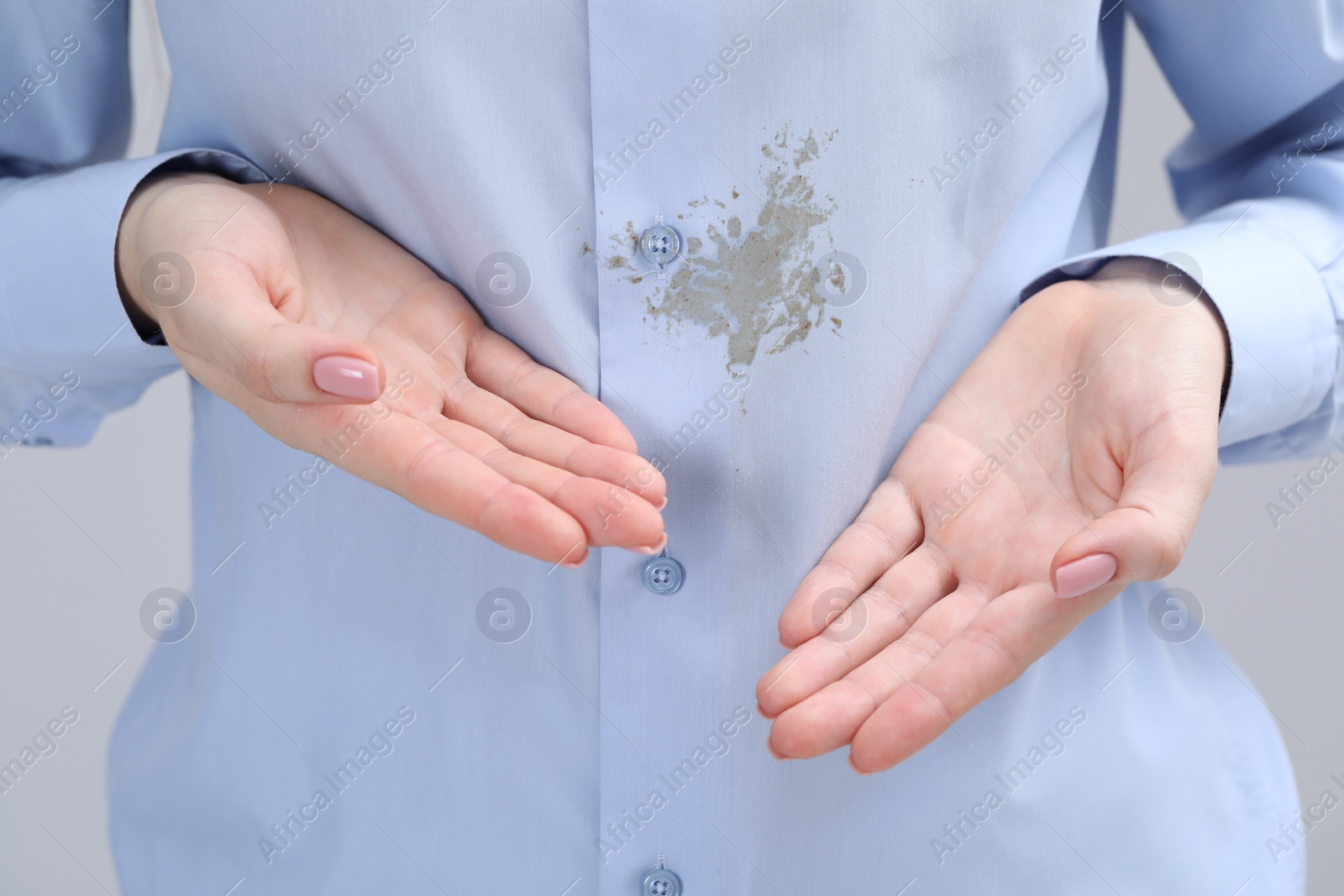 Photo of Woman showing stain on her shirt against light grey background, closeup