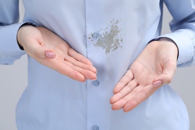 Woman showing stain on her shirt against light grey background, closeup