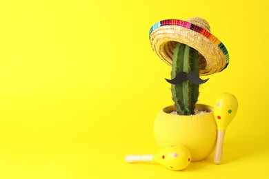 Cactus with Mexican sombrero hat, fake mustache and maracas on yellow background, space for text