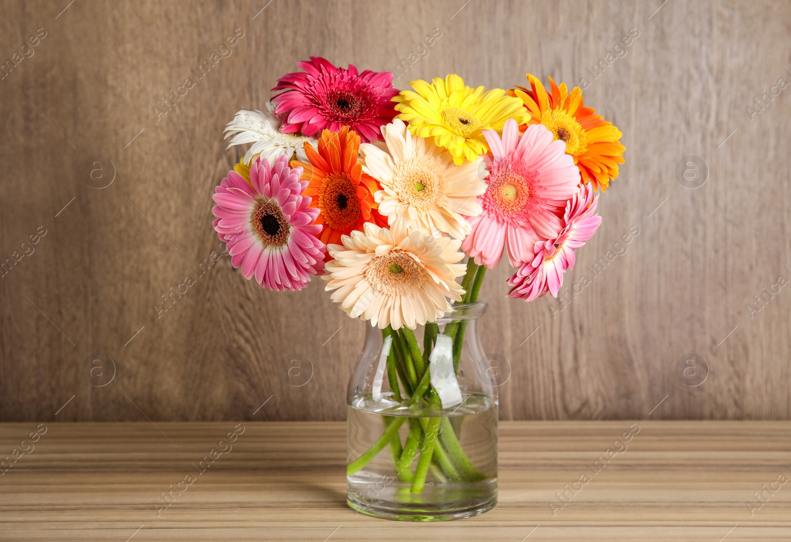 Photo of Bouquet of beautiful bright gerbera flowers in glass vase on table against wooden background
