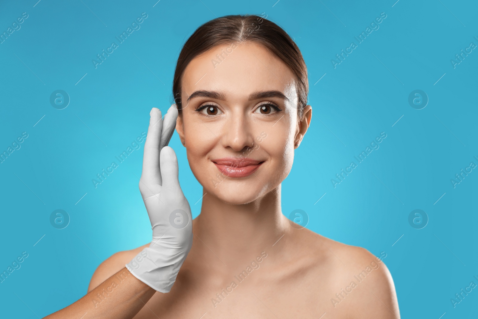 Photo of Doctor examining woman's face before plastic surgery on light blue background