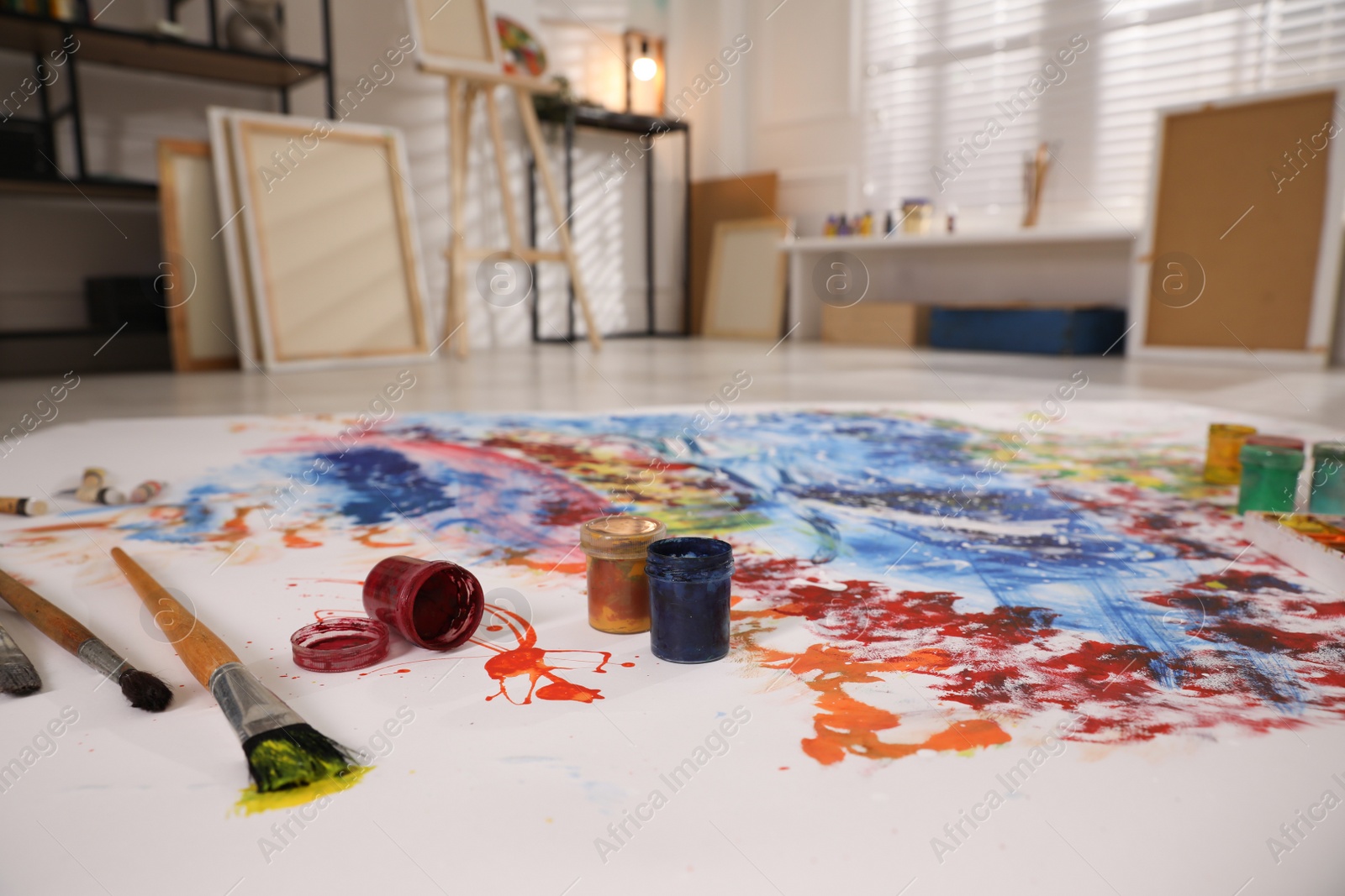 Photo of Paints and brushes on abstract picture in art studio with easel