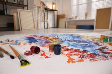 Photo of Paints and brushes on abstract picture in art studio with easel