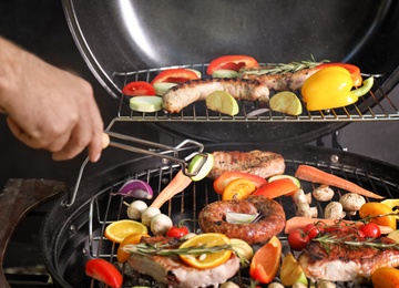 Photo of Man cooking delicious meat and vegetables on barbecue grill, closeup