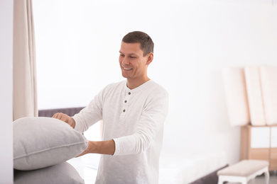 Photo of Happy man choosing cushion in mattress store