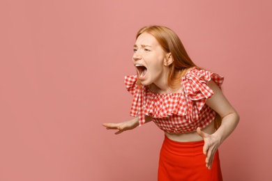 Portrait of angry screaming woman on pink background, space for text