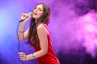 Photo of Emotional woman with microphone singing in color lights. Space for text