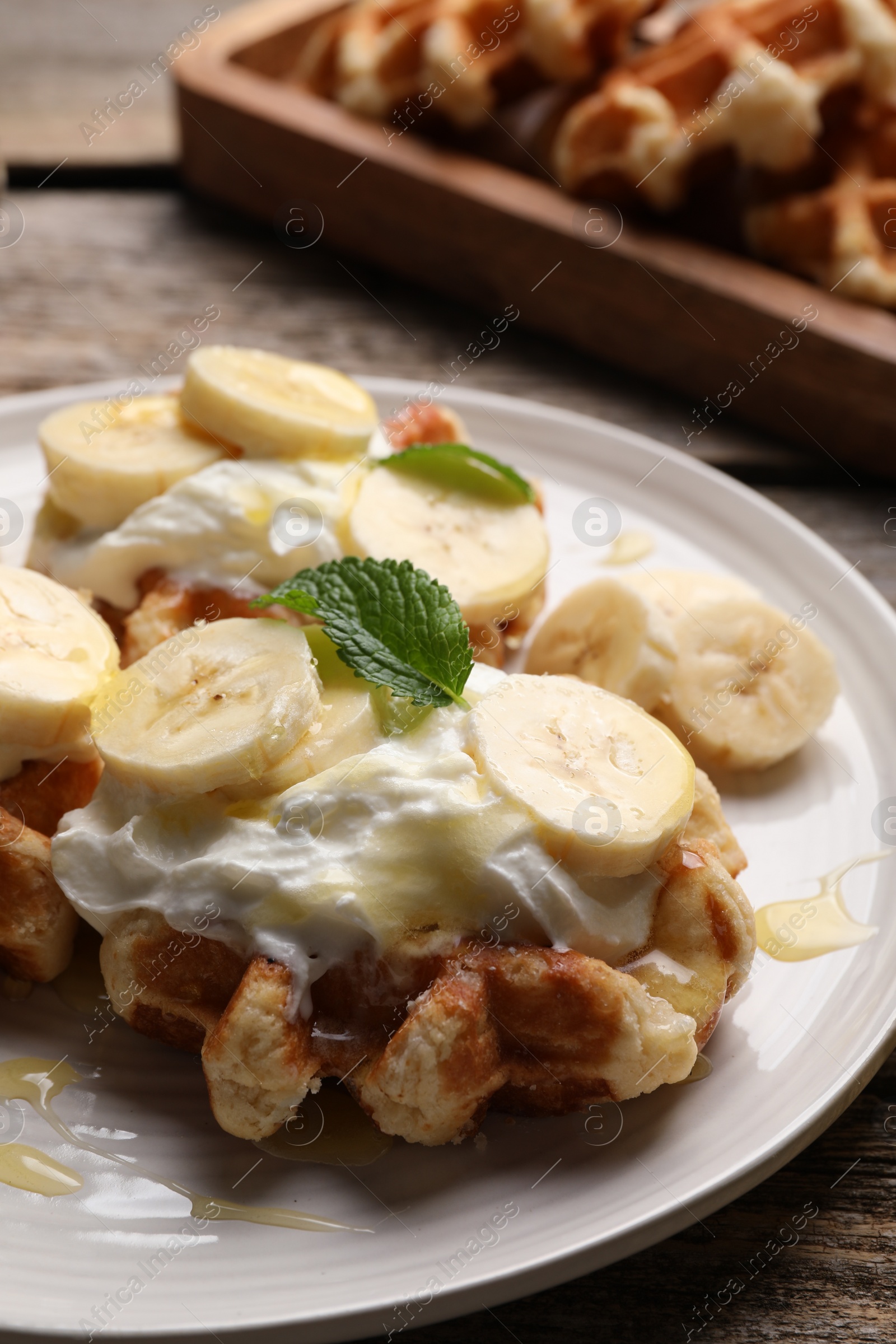 Photo of Delicious Belgian waffles with banana and whipped cream on table, closeup