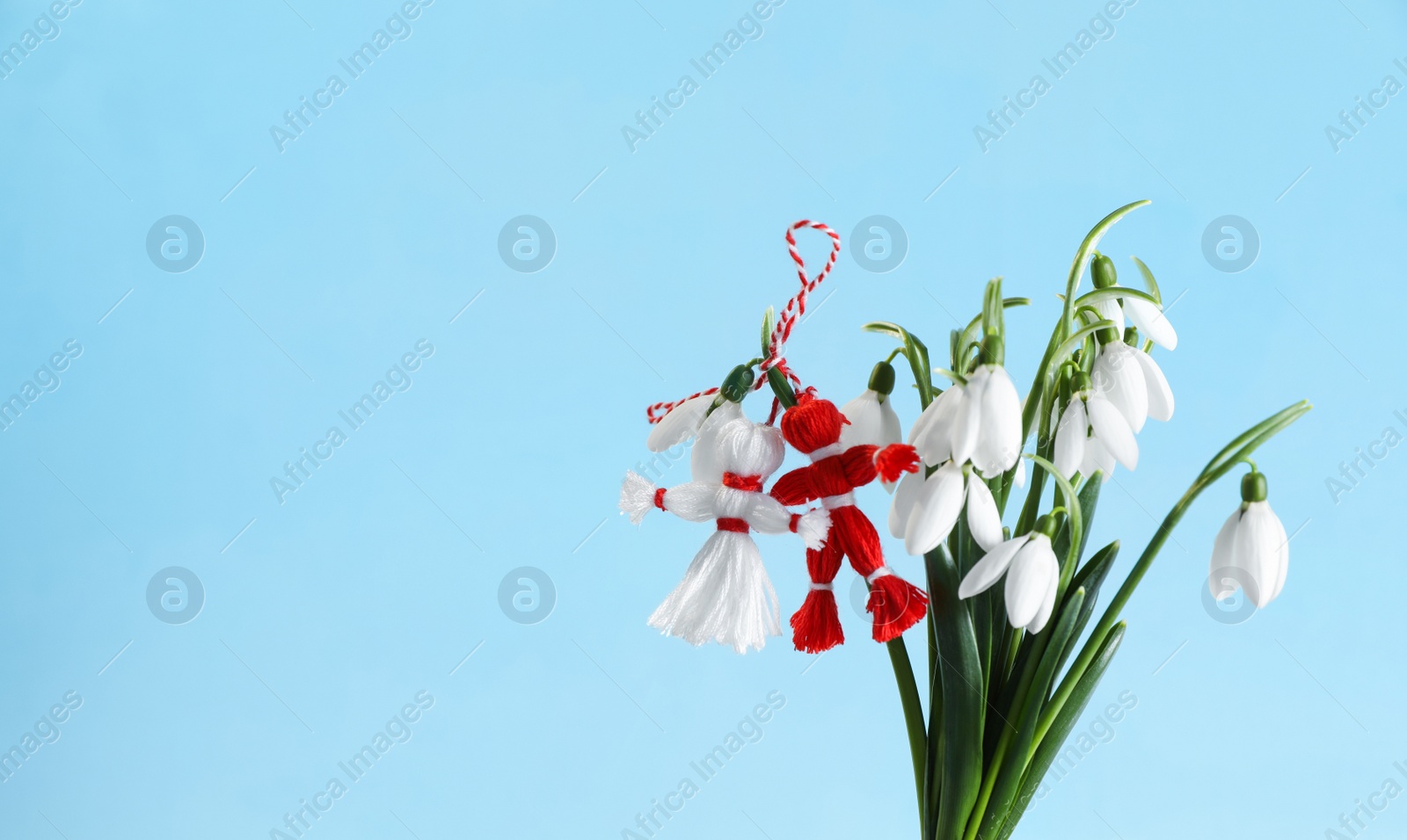 Photo of Traditional martisor and beautiful snowdrops on light blue background, space for text. Symbol of first spring day