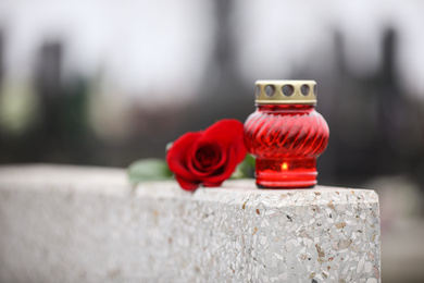 Photo of Red rose and candle on light grey granite tombstone outdoors. Funeral ceremony