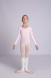 Photo of Little ballerina practicing dance moves on grey background