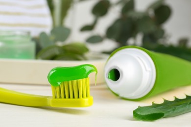 Photo of Toothbrush with toothpaste and fresh aloe leaf on white wooden table, closeup