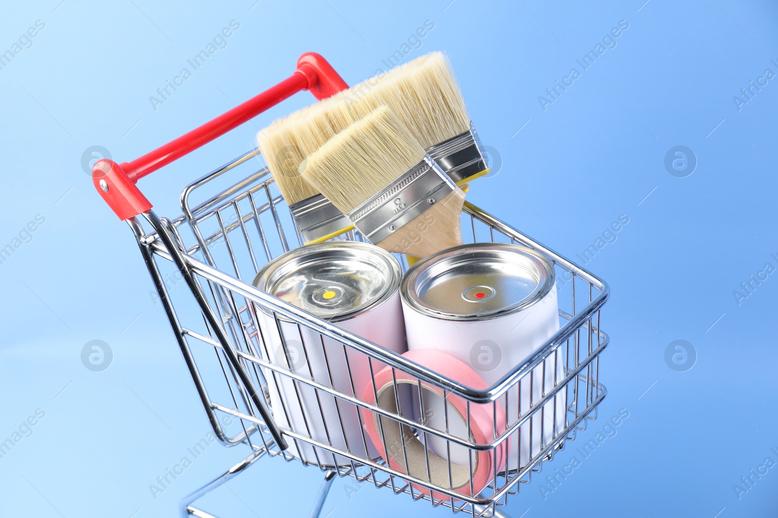 Photo of Small shopping cart with set of painting tools on light blue background