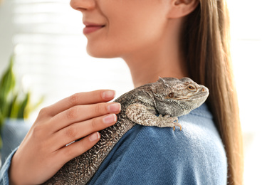 Photo of Young woman with bearded lizard at home, closeup. Exotic pet