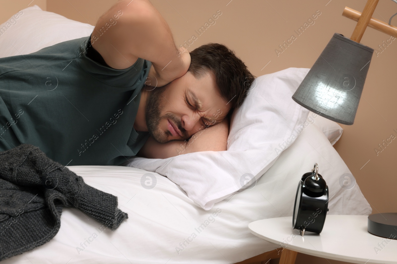 Photo of Sleepy man covering his ears with hands in bed at home
