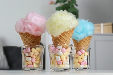 Sweet cotton candies in waffle cones and marshmallows on white table indoors, closeup