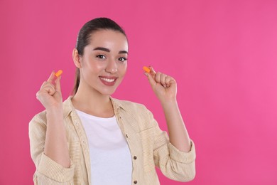 Photo of Young woman inserting foam ear plugs on pink background. Space for text