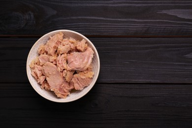 Photo of Bowl with canned tuna on black wooden table, top view. Space for text