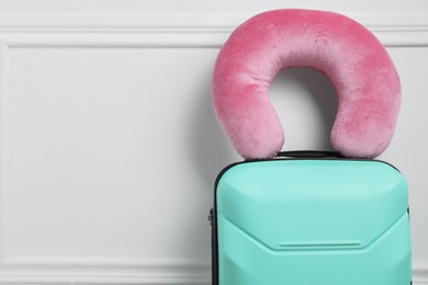 Photo of Pink travel pillow on turquoise suitcase near white wall, space for text