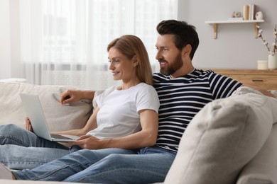 Happy couple with laptop on sofa at home