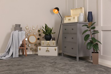 Photo of Stylish room interior with storage trunks, grey chest of drawers and plants