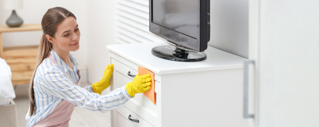 Young chambermaid wiping dust from furniture in hotel room. Banner design