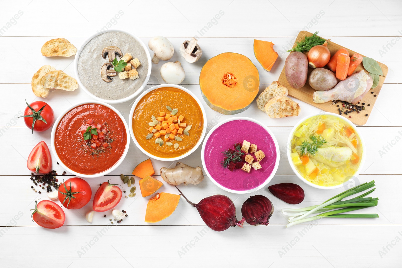 Photo of Tasty broth, different cream soups in bowls and ingredients on white wooden table, flat lay