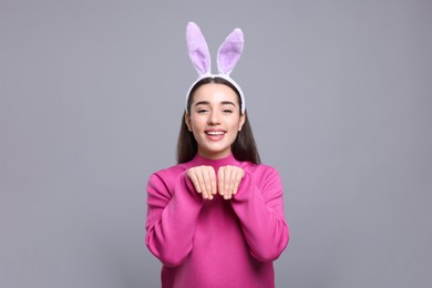 Photo of Happy woman wearing bunny ears headband on grey background. Easter celebration