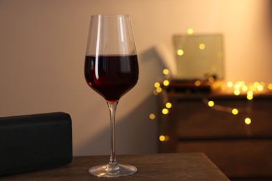 Glass of red wine and loud speaker on wooden table in room, space for text. Relax at home