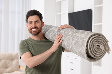 Smiling man holding rolled carpet in room